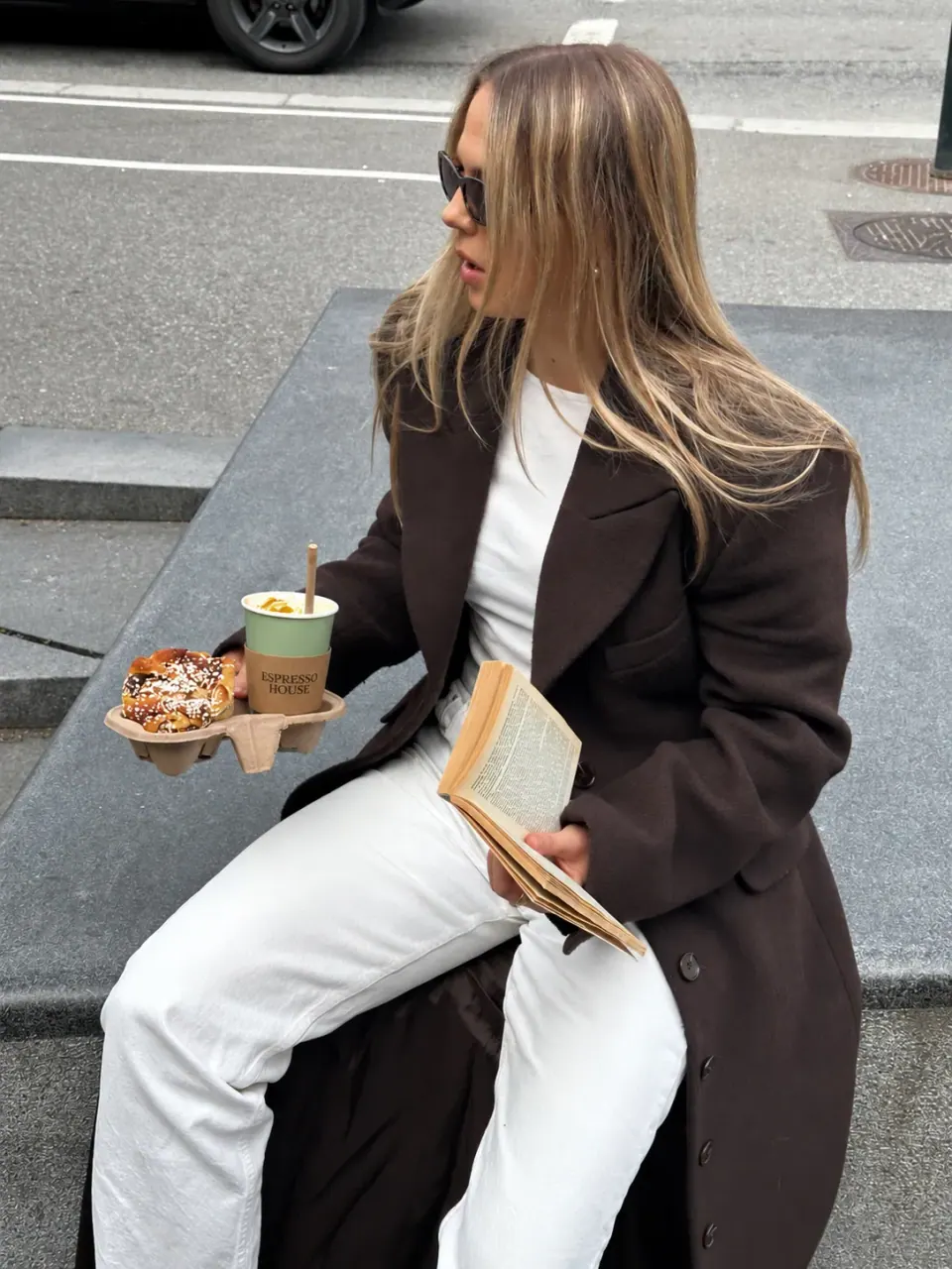 Creator holding coffee and a snack outside a café